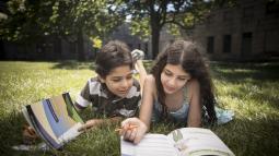 A boy and a girl lying on the grass working on junior ranger books.