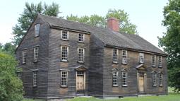 A wooden colonial era house with multiple stories and windows