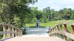 Standing in the middle of a wooden bridge with railings on either side, looking toward a statue.