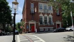 Brick building on street corner with three arched windows in center.