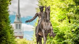 A metal statue of Paul Revere on horseback stands in front of the steeple of Old North Church.