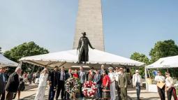 A group photo of people standing around two wreaths with the Bunker Hill Monument in the background.