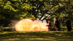 A cannon firing with a massive flame shooting out the muzzle of the gun.